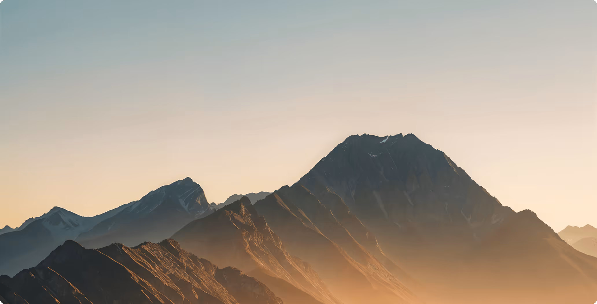 Sunset-lit mountain range with sharp peaks under a clear sky.