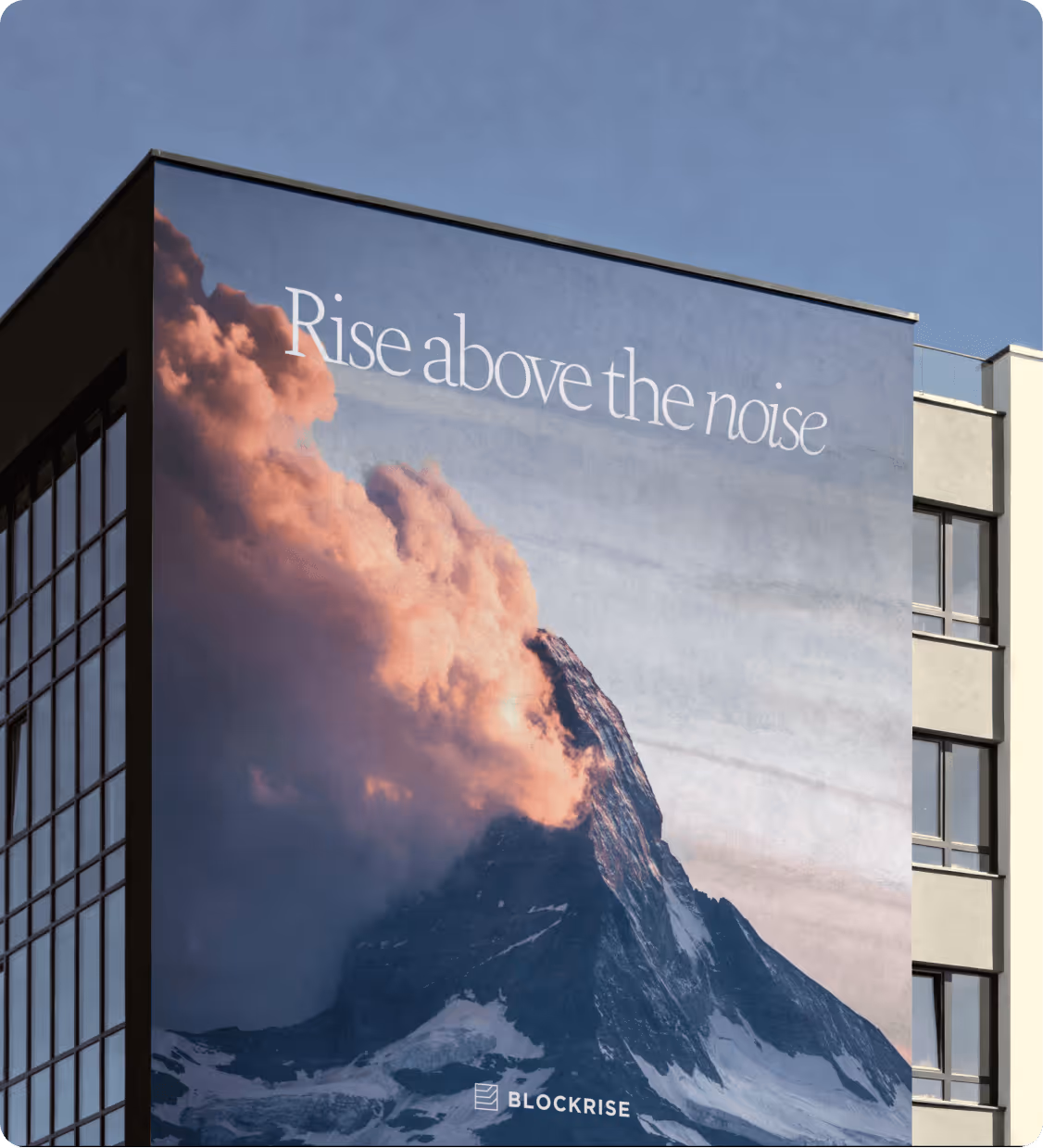Building side with a large mural of a mountain peak partially covered by clouds and the text 'Rise above the noise.'