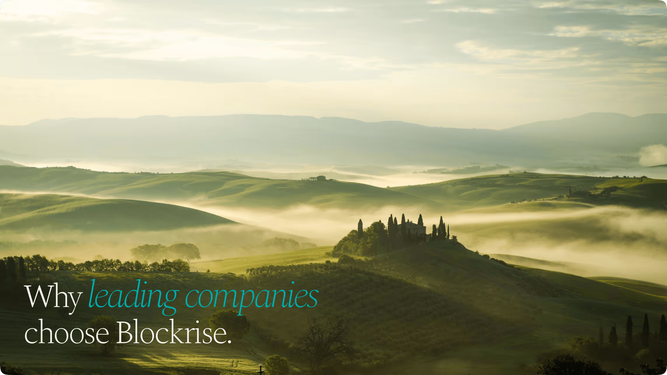 Mist-covered rolling green hills with a group of tall trees and a building on a hilltop under a cloudy sky.