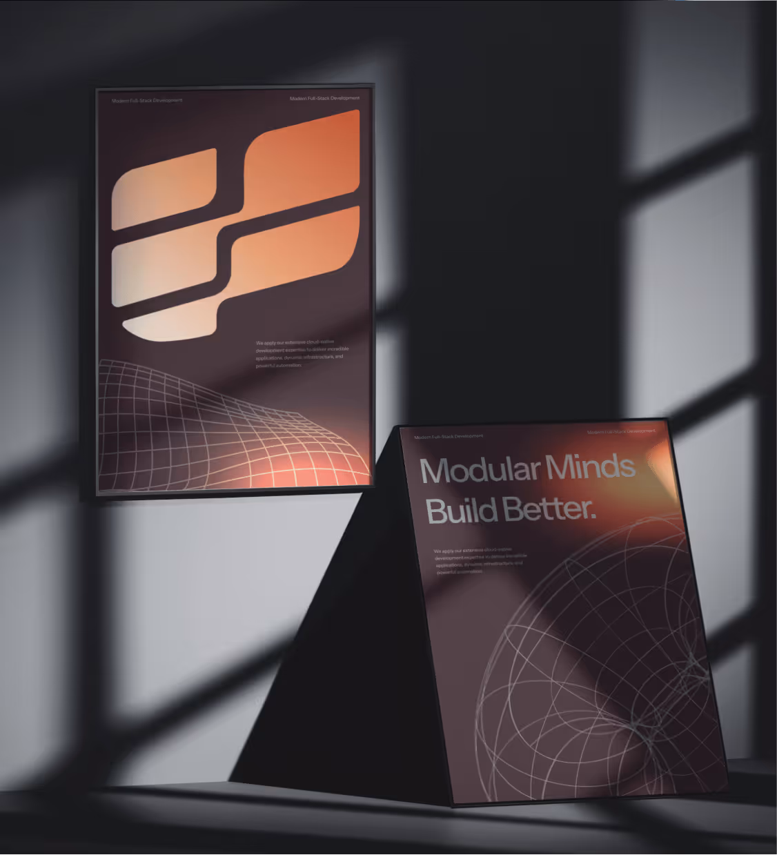 Two posters with gradient orange abstract designs and text, one hanging on a wall and one standing on a triangular base casting shadows.