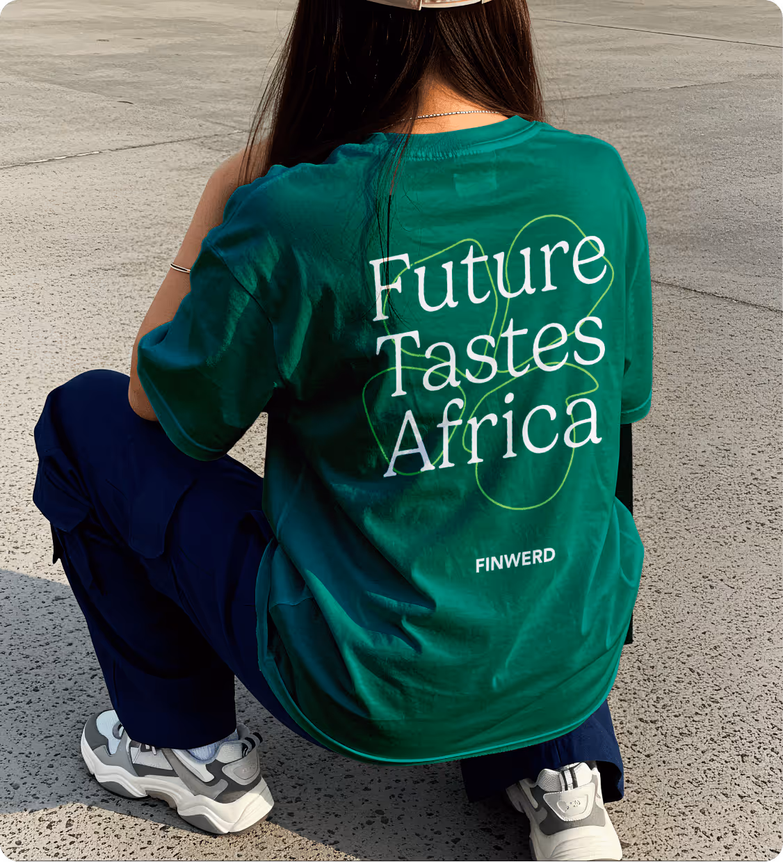 Person crouching on concrete wearing a green shirt with text 'Future Tastes Africa' and dark pants.