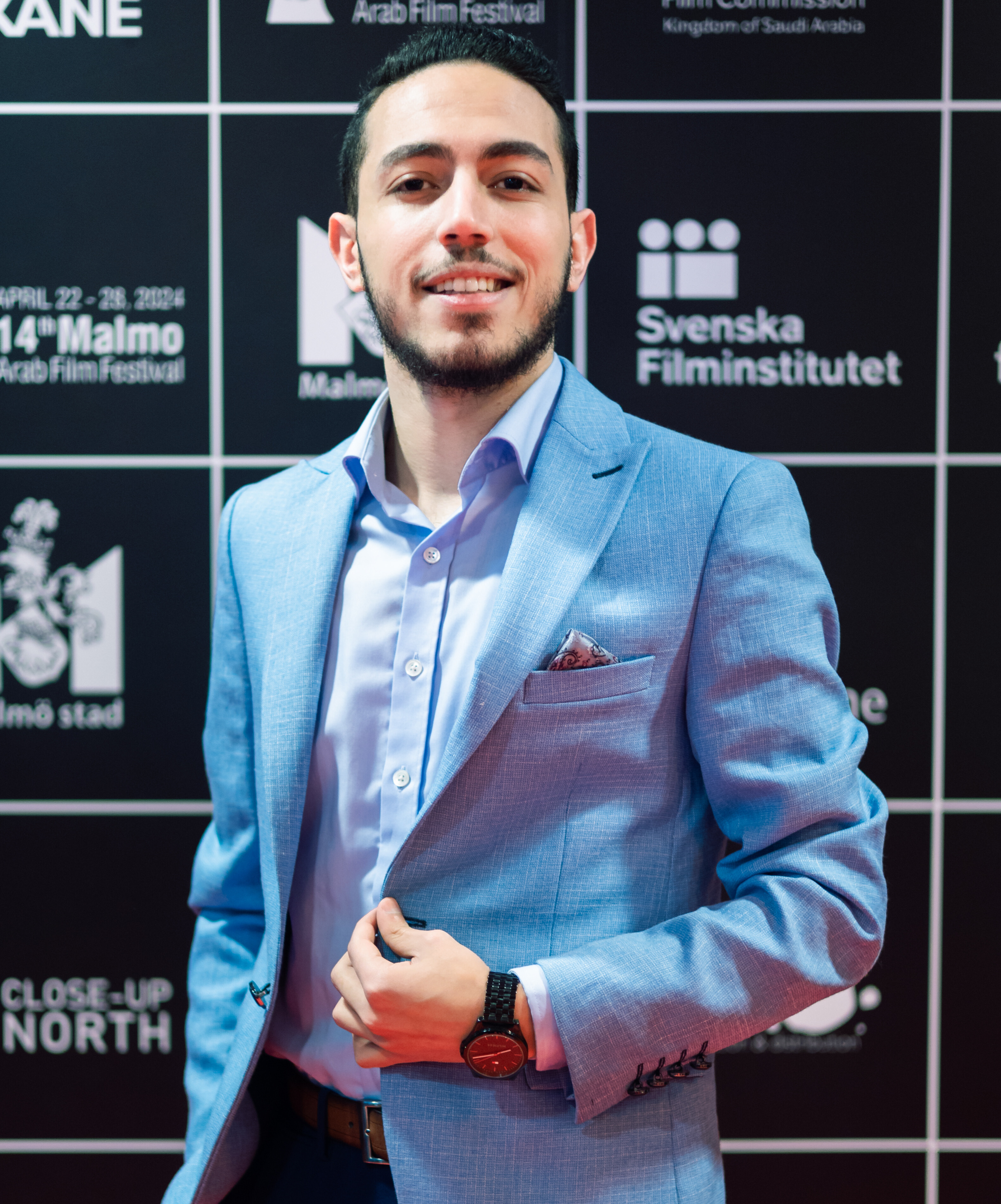 Man in light blue blazer and shirt smiling in front of a film festival backdrop.