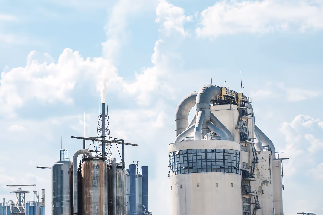 Industrial facility with large metal tanks and pipes emitting white smoke against a partly cloudy sky.