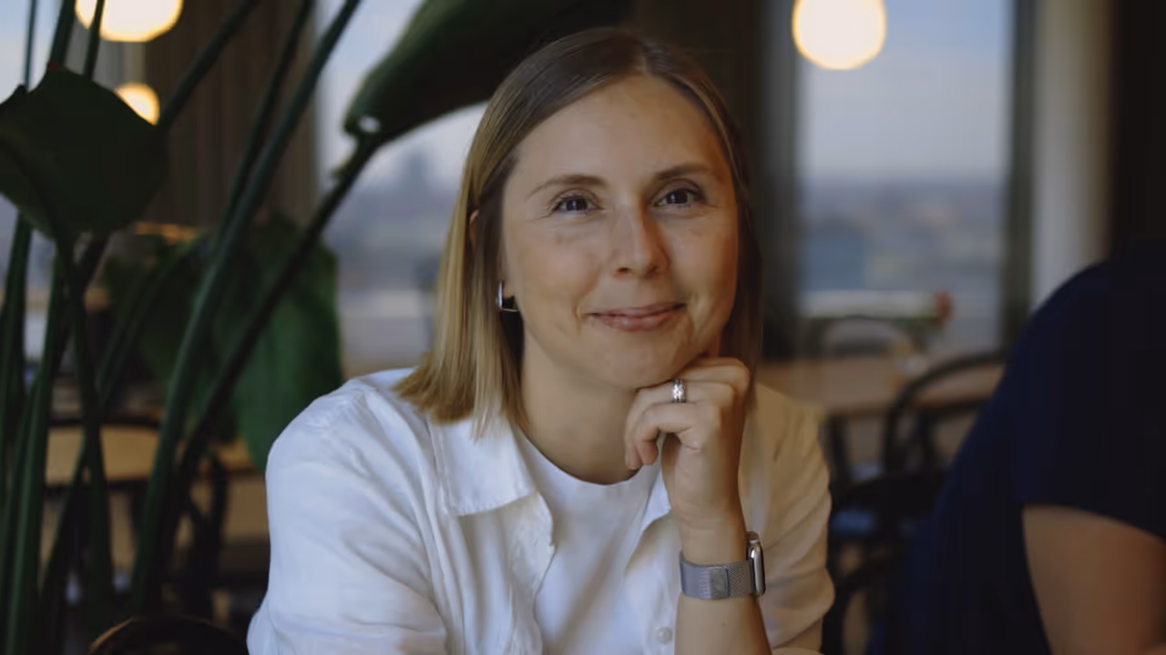 Smaidoša gaišmataina sieviete ar baltu kreklu pieskauj zodu pie rokas atpūtas telpā.
