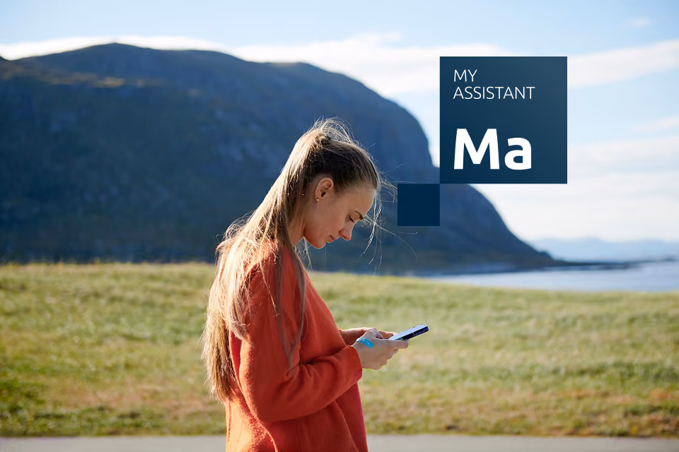 Sieviete lauku ainavā skatās uz viedtālruni, izmantojot Jumis My Assistant risinājumu.