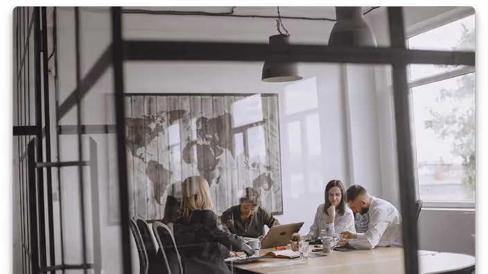 A team in a meeting working with computers and documents at a table.