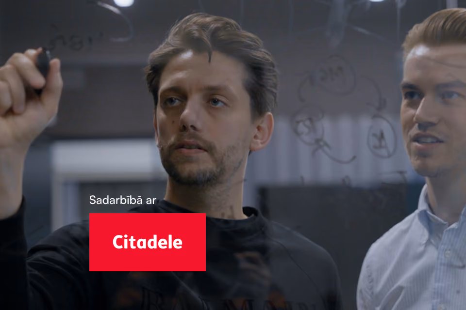 Divi kolēģi raksta idejas uz stikla tāfeles.
