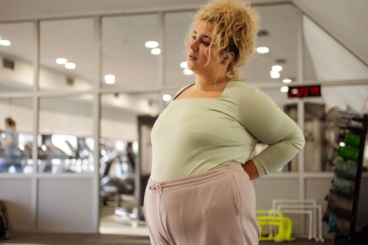 Frau mit grünem Shirt hat Rückenschmerzen wegen Übergewicht