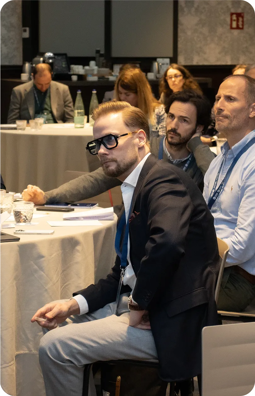 Group of people seated at round tables attentively listening in a conference or seminar.