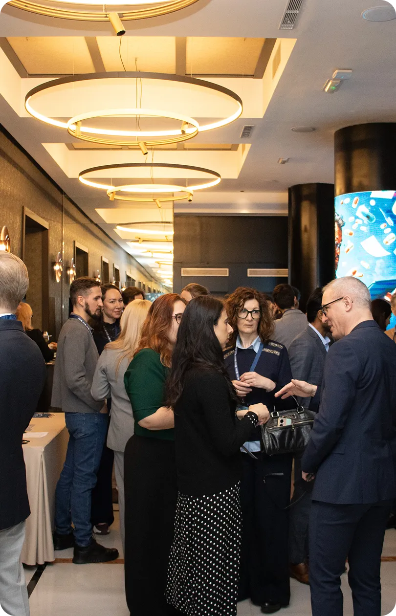 Group of people engaged in conversation at a professional networking event in a modern indoor space with circular ceiling lights.