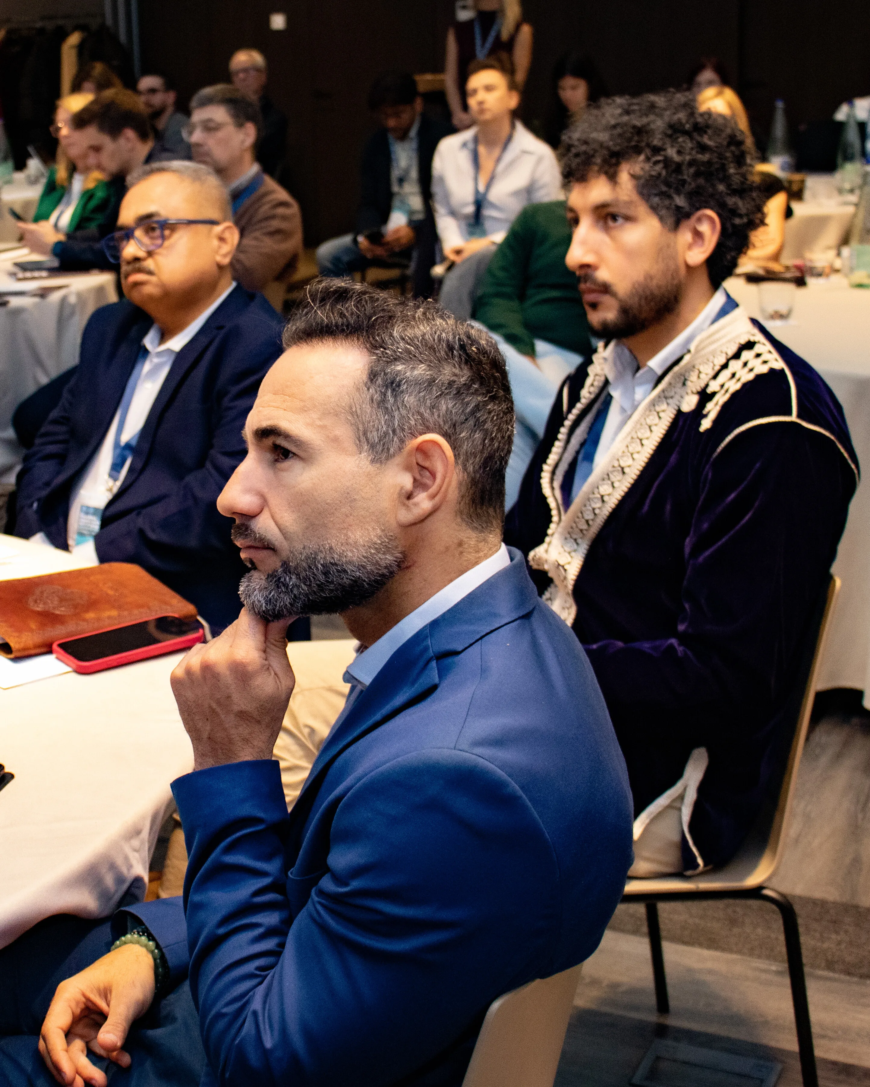 Attentive diverse group of adults seated at round tables in a conference setting.