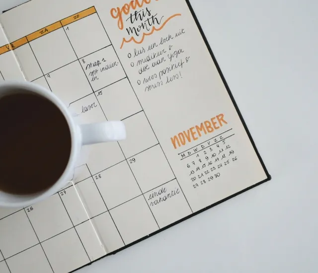 Open bullet journal showing a November calendar with handwritten notes and a cup of coffee on the left side.