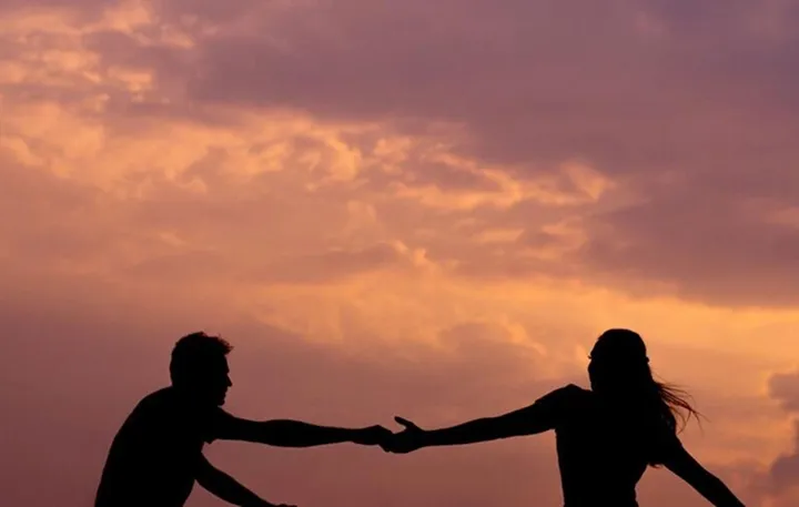 Two people shaking hands against a white background, one wearing a checkered vest.