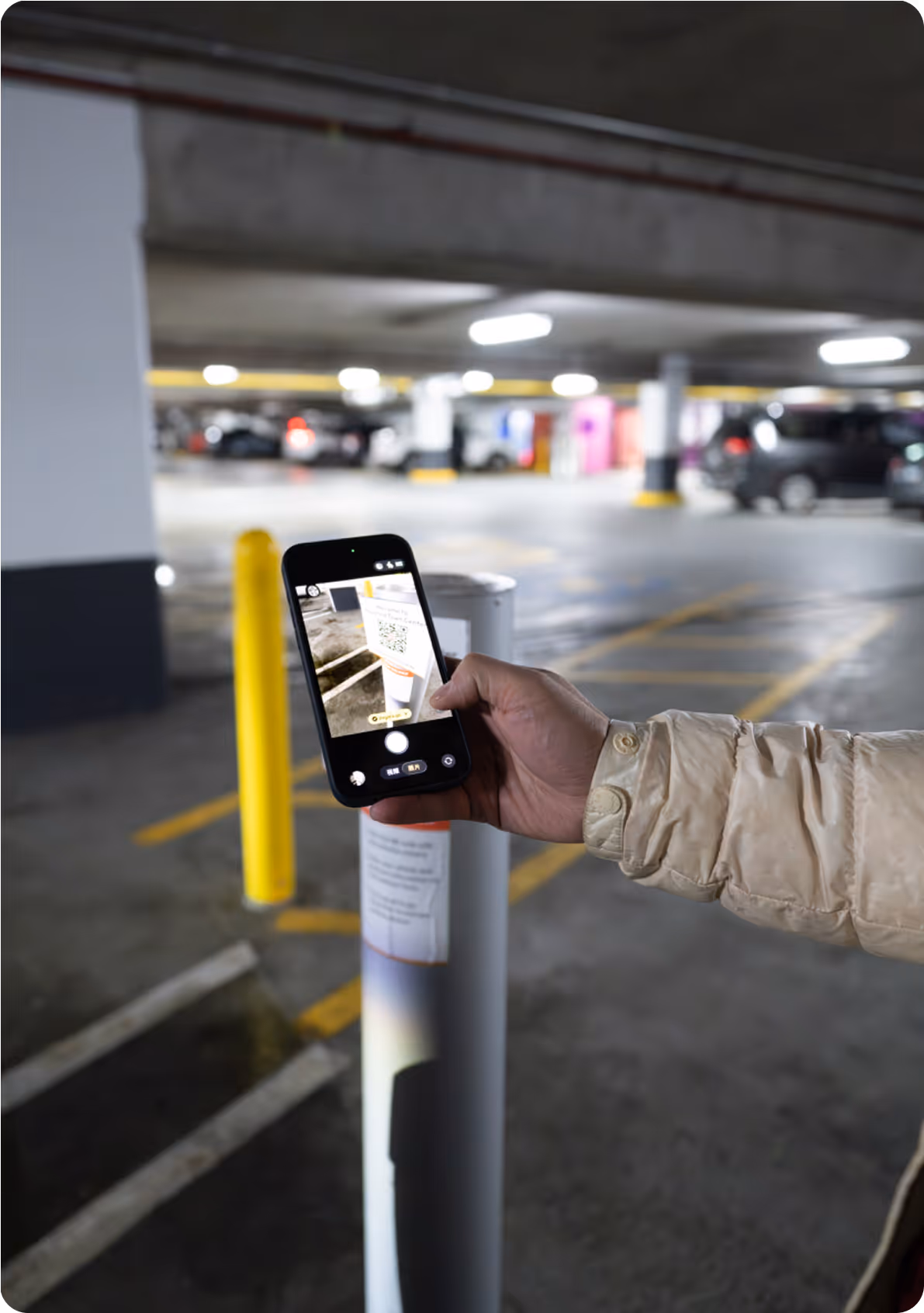 Person uses smartphone to scan QR code on a white pole in a dimly lit parking garage.