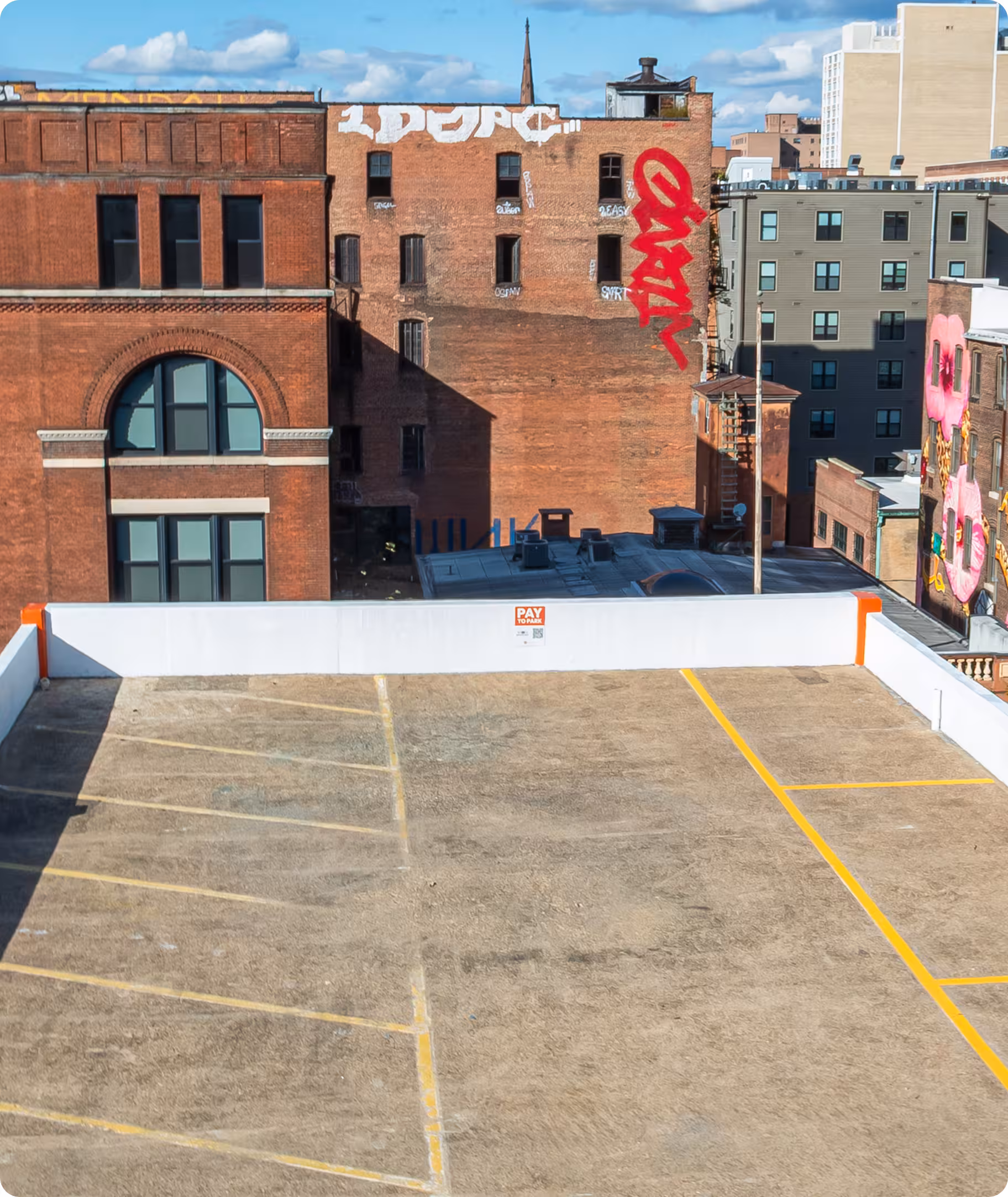 Empty rooftop parking lot with yellow lines against urban buildings and blue sky background.