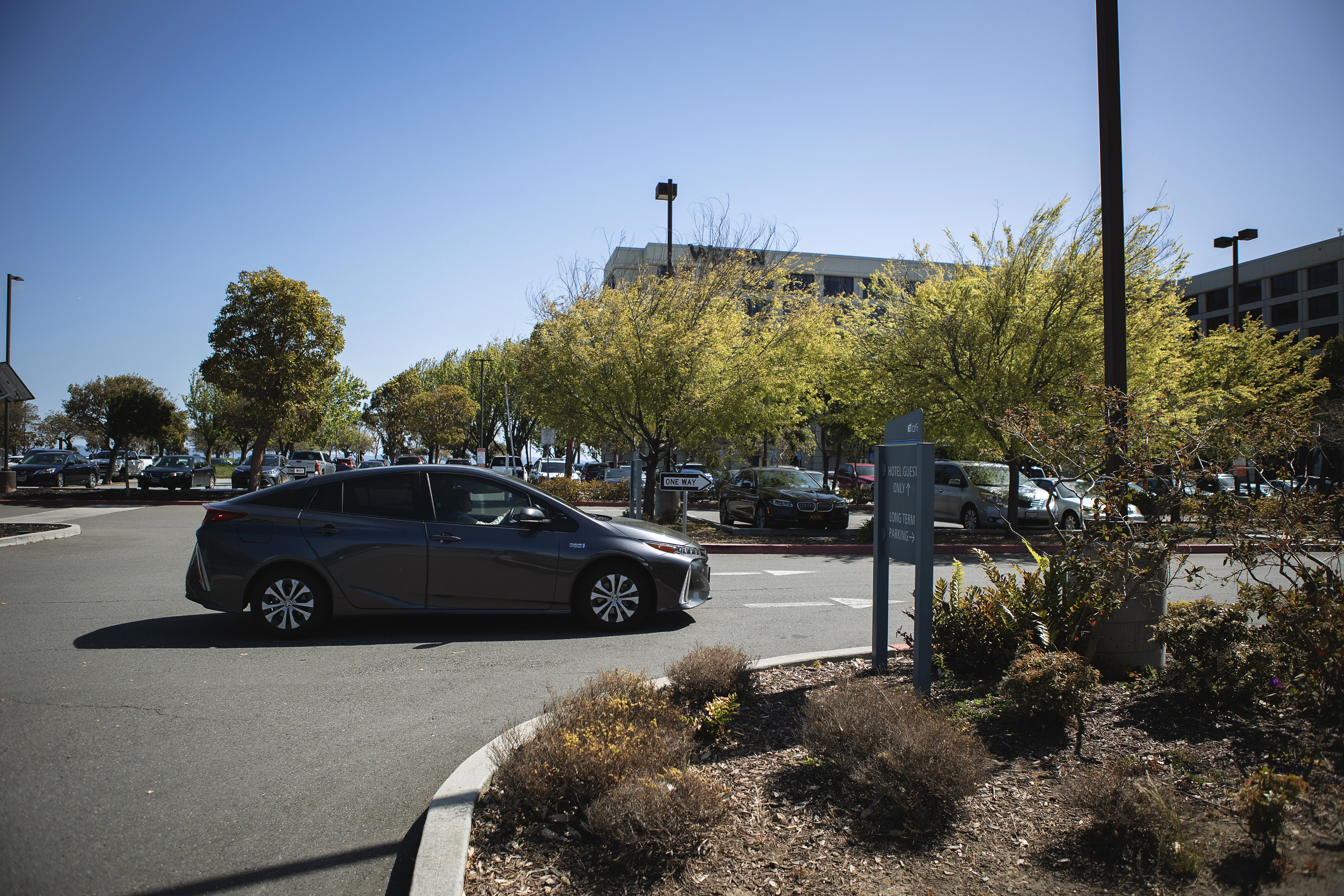 Gray sedan driving on a road near trees and a sign indicating hotel guest and long-term parking.