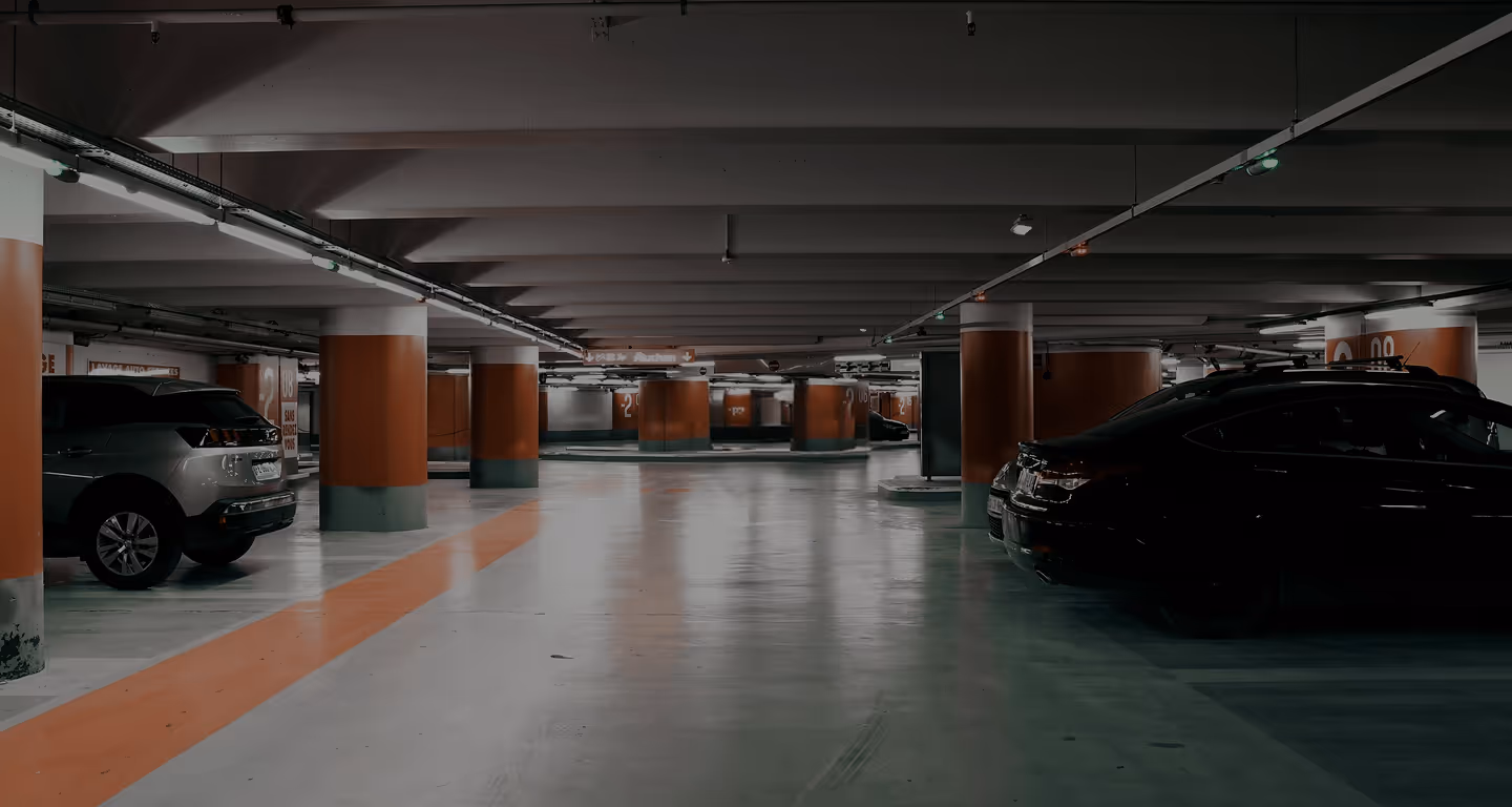 Empty underground parking garage with orange pillars and parked cars on sides.