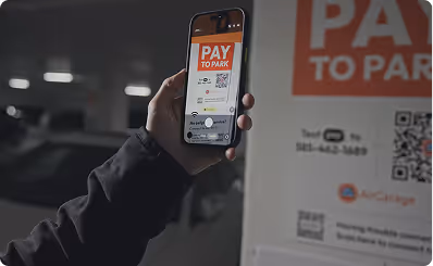 Hand holding phone displaying a 'Pay to Park' app with QR code in a parking area at night.