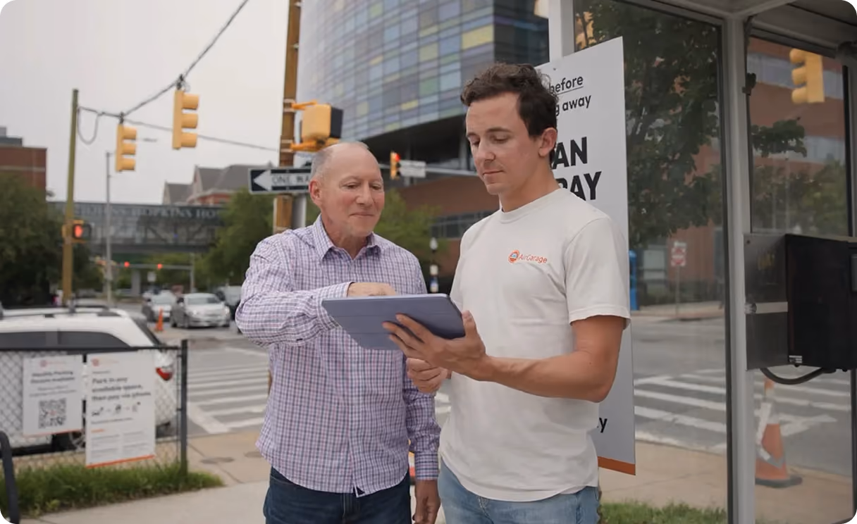 Two men standing outside in a city, one holding a clipboard while the other points at it.