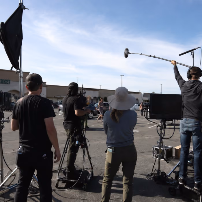 Film crew with camera, boom mic, and monitor filming a scene in an outdoor parking lot