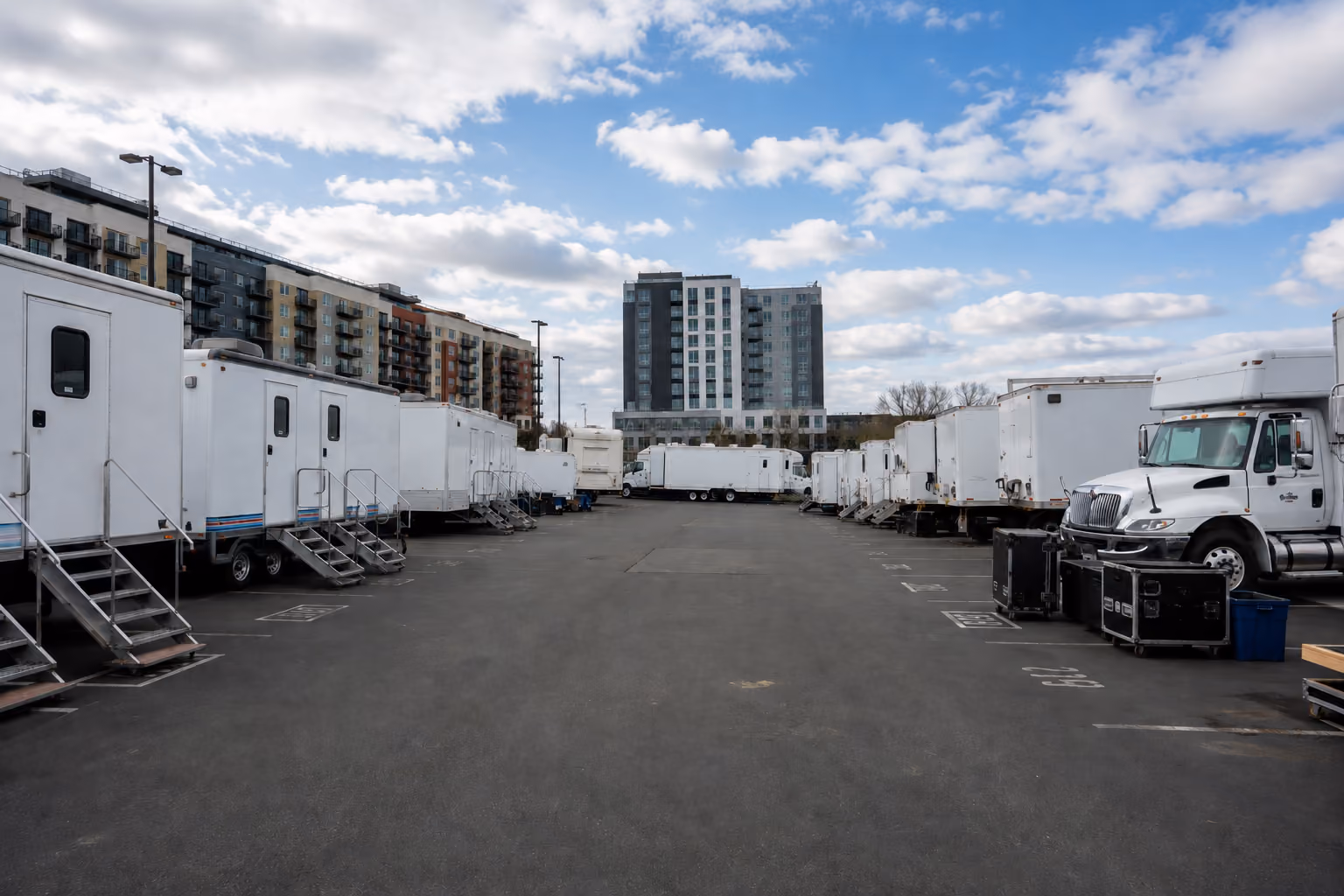 Rows of production trailers and trucks parked in an outdoor lot with apartment buildings in the background