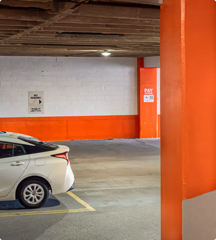 Indoor parking garage with a car parked near Pay to Park and No Parking signs on orange and white walls