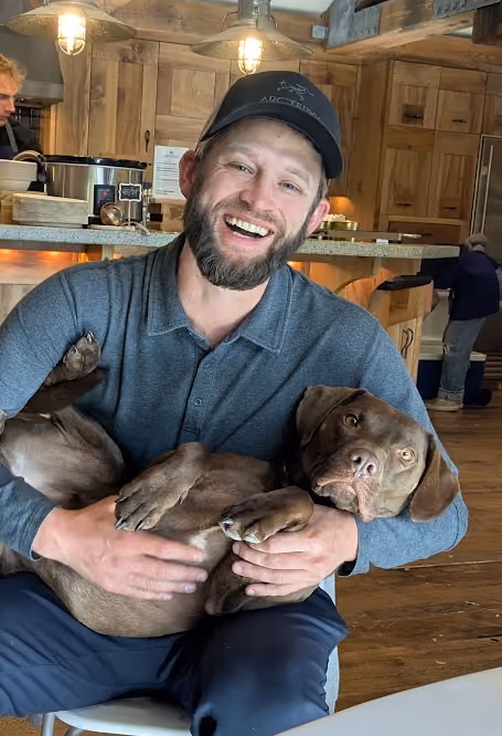 Man smiling and holding a brown dog in a rustic kitchen setting