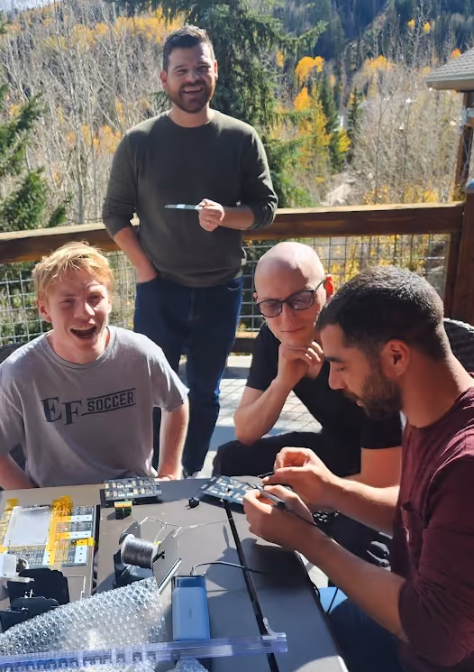Team members soldering electronic hardware components together on an outdoor deck