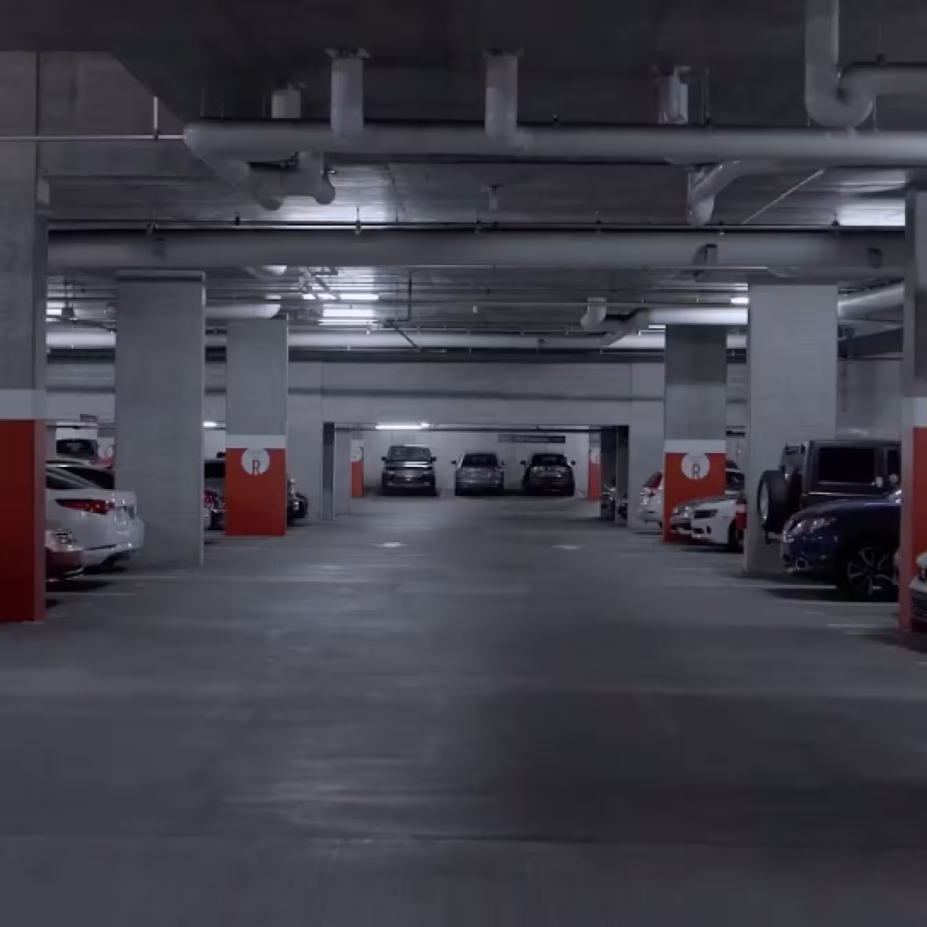 Cars parked in an underground parking garage with concrete columns and overhead pipes