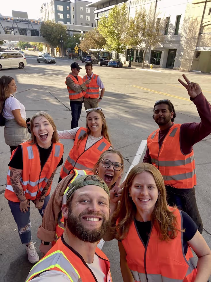 Group of team members wearing orange safety vests smiling together on a city street