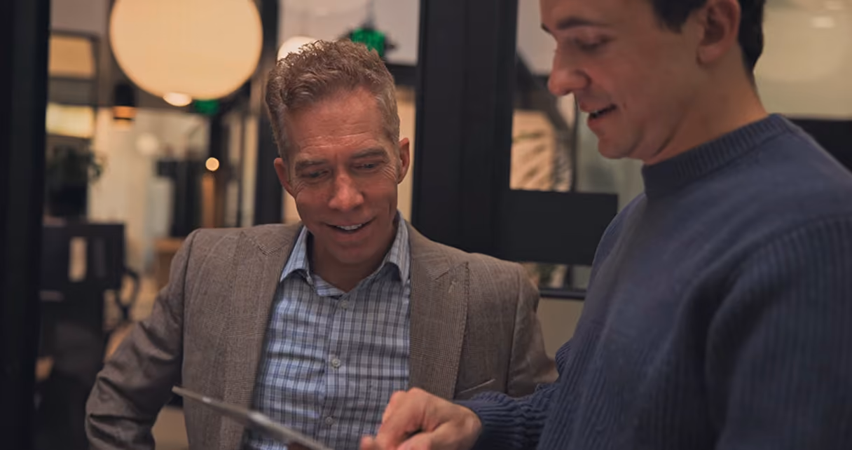 Two men reviewing information together on a tablet in an office setting