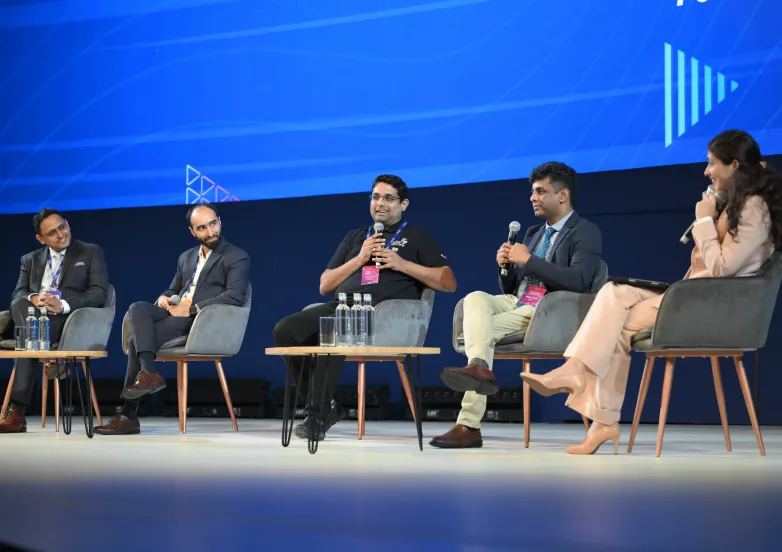 Five panelists seated on stage, two men holding microphones speaking during a discussion.