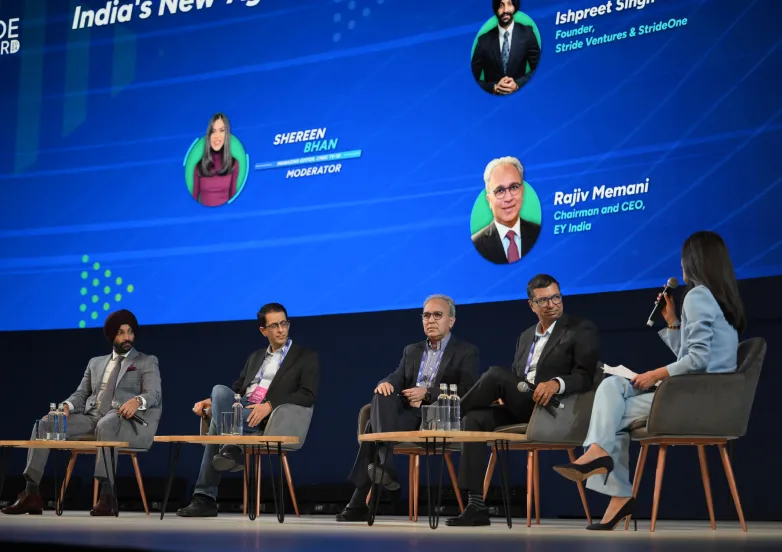 Panel discussion with five professionals seated on stage, one speaking into a microphone in front of a blue digital backdrop.