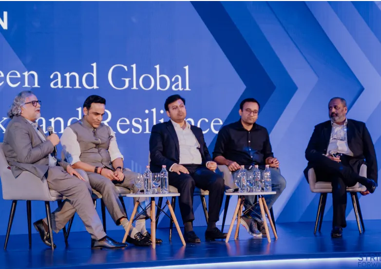 Five men seated on stage in a panel discussion with water bottles on tables against a blue backdrop.