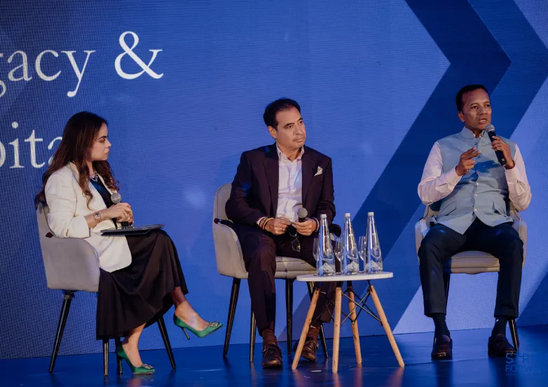 Three people sitting on chairs on stage, two men and one woman, speaking into microphones.