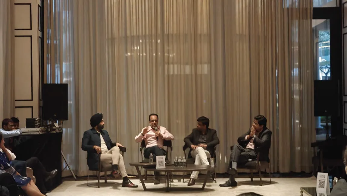 Four men seated on chairs having a panel discussion in front of a curtain in a conference room.