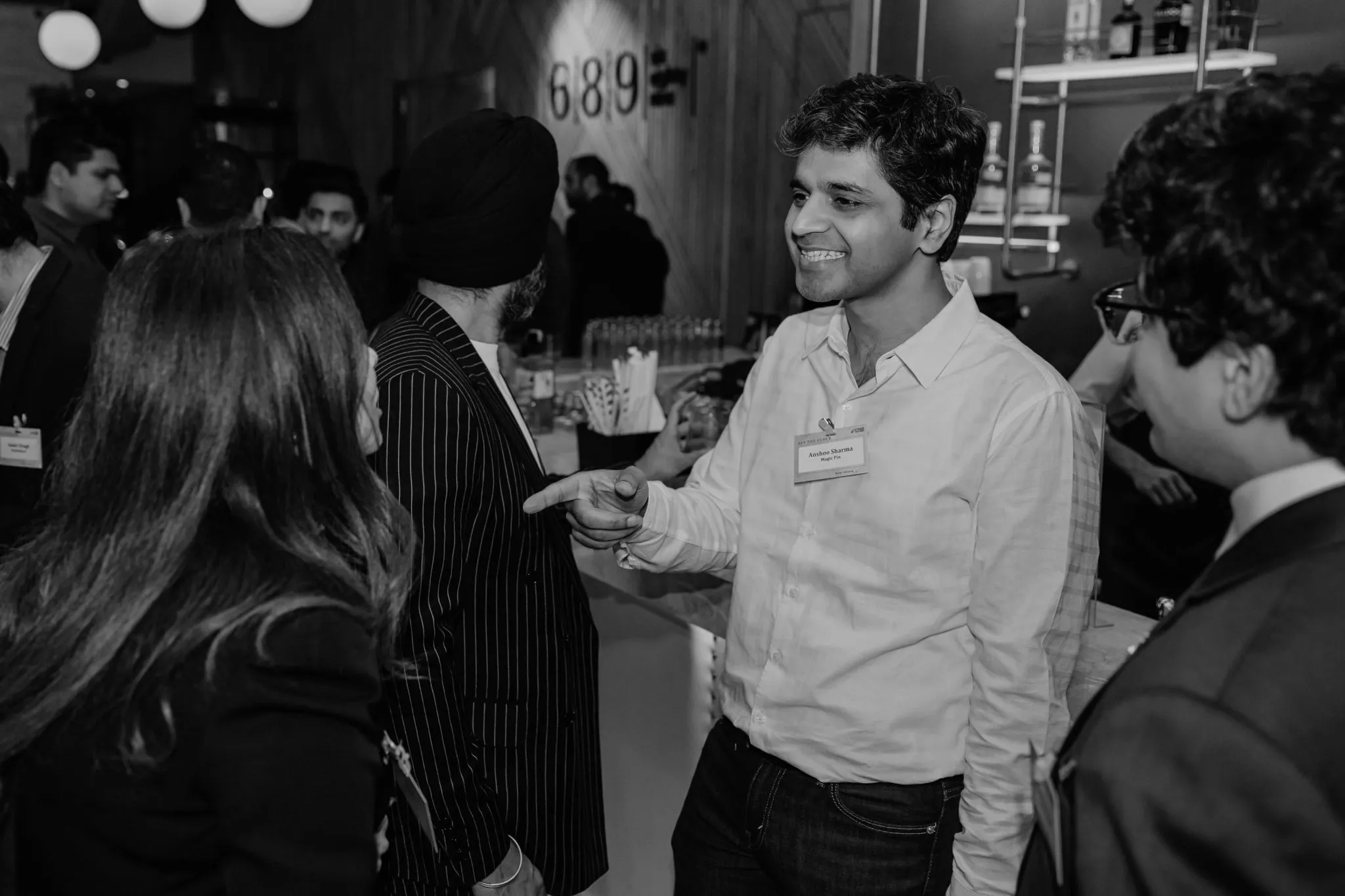 Group of people socializing indoors, one man smiling and pointing while others listen attentively.