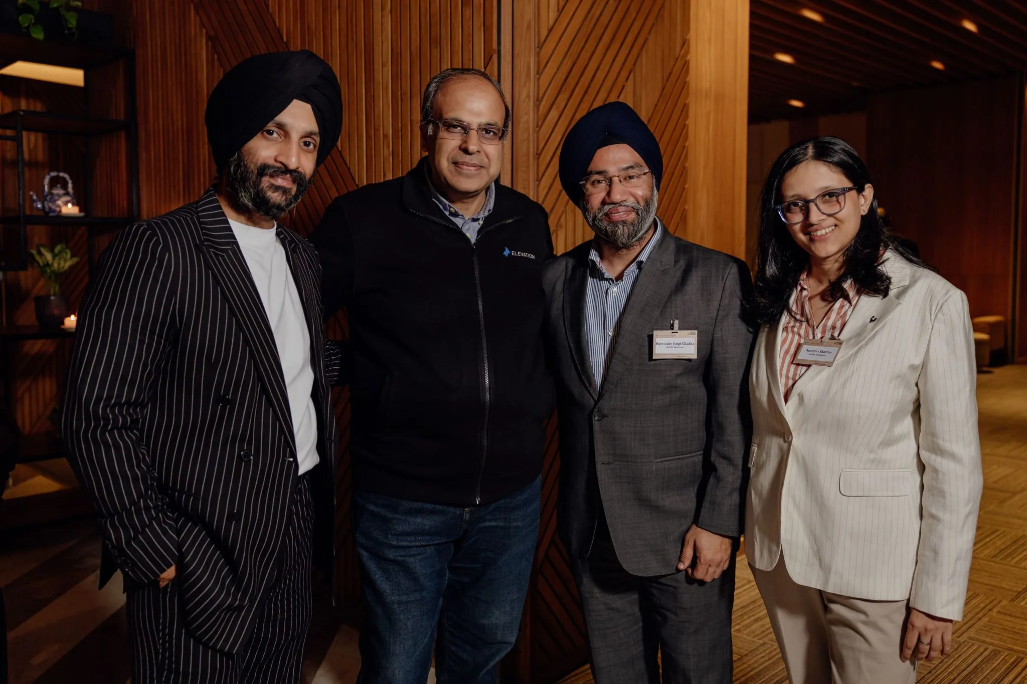 Four people dressed in business attire posing and smiling indoors with wooden paneled background.