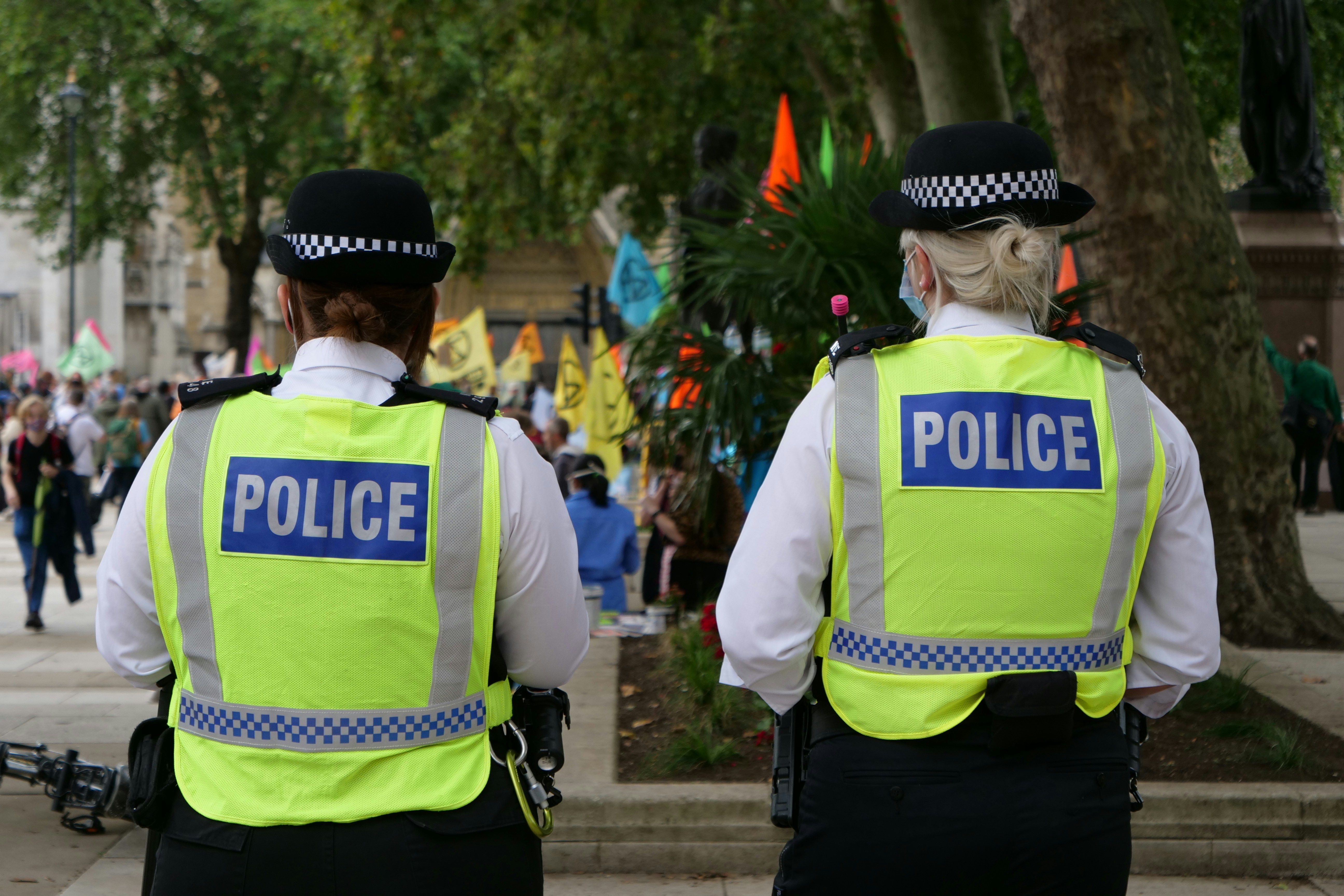 Two police officers in high-visibility jackets observing a crowd with colorful flags at an outdoor event.