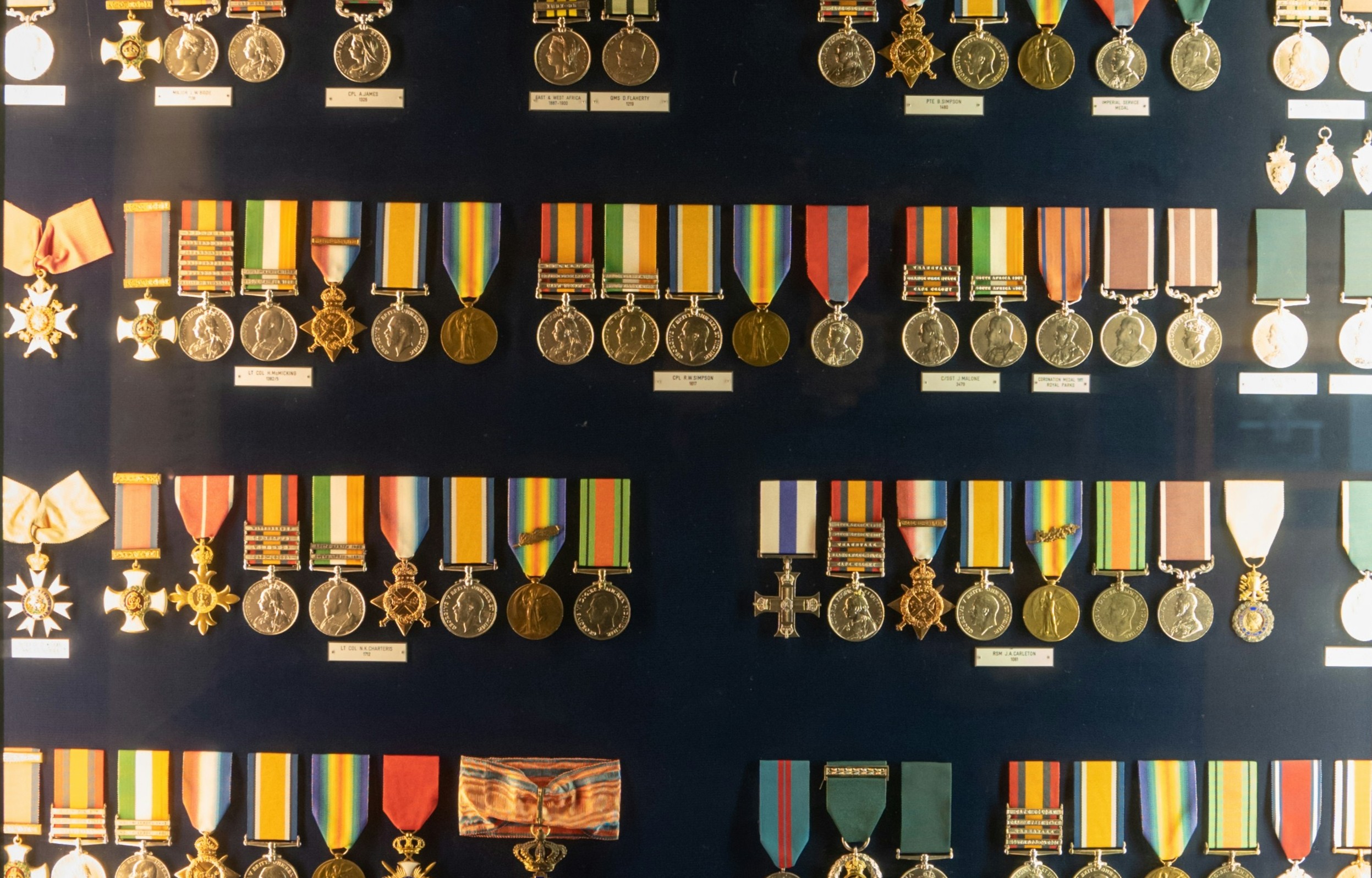 Display case of various military medals and decorations arranged in rows against a dark background.