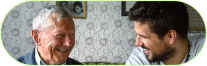 Älterer Mann und jüngerer Mann lachen gemeinsam bei einem Gespräch in einem gemütlichen Zimmer.