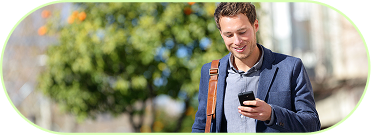 Junger Mann mit blauem Sakko und Lederschultertasche schaut lächelnd auf sein Smartphone im Freien.