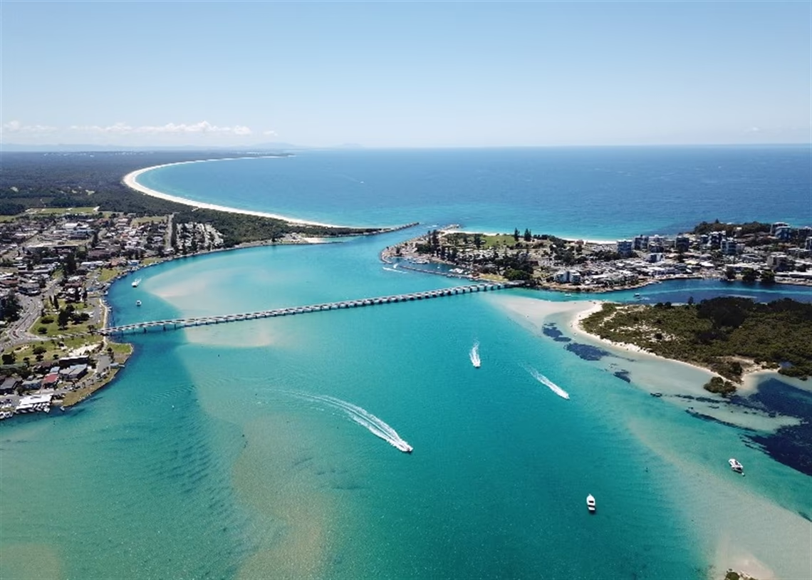 Aerial view of coastal town with bridge over turquoise water and boats near sandy beaches.