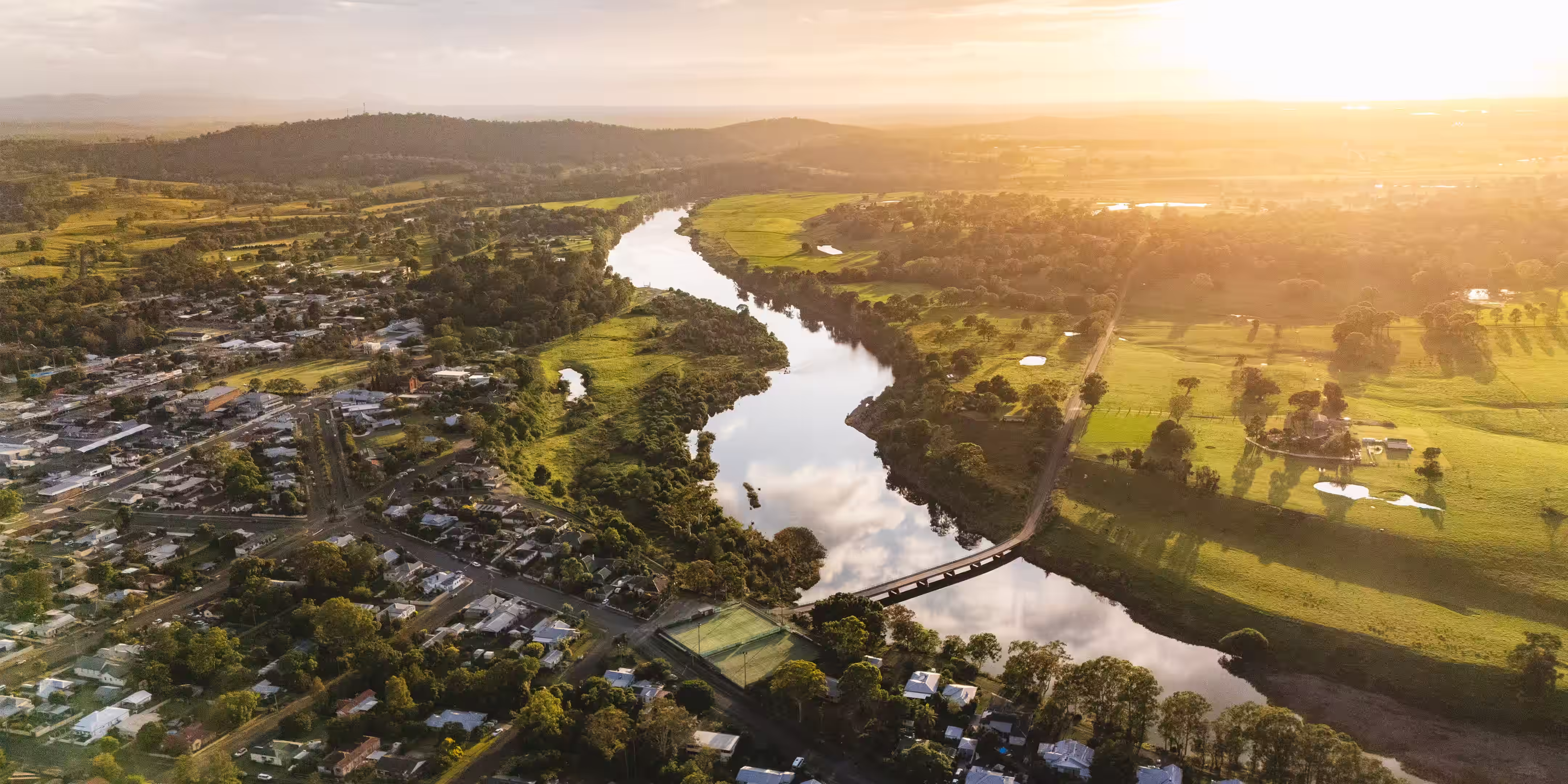 Sunset over a river winding through farmland and a small town with scattered trees and hills.