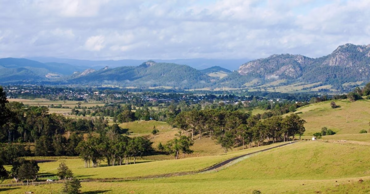 Rolling fields with clusters of trees and distant mountains under a cloudy sky.