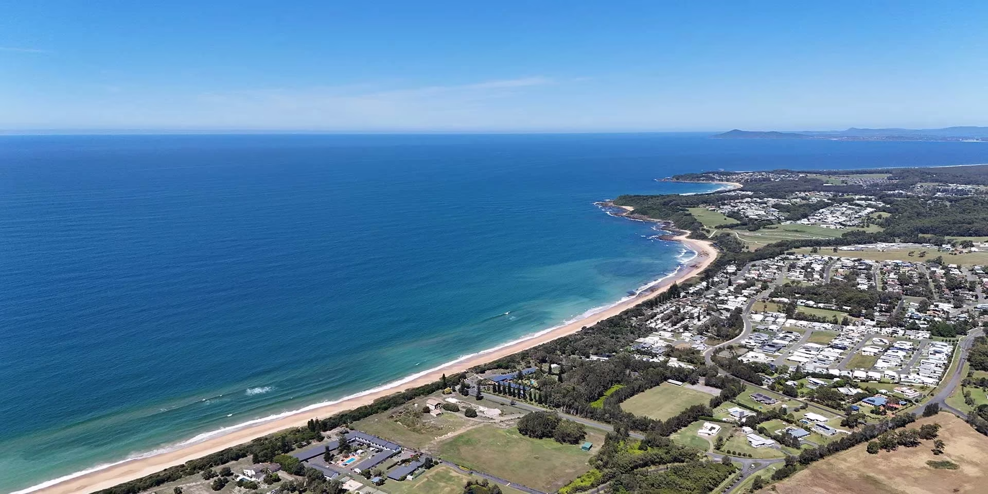 Aerial view of a coastline with blue ocean, sandy beach, and residential areas near the shore.