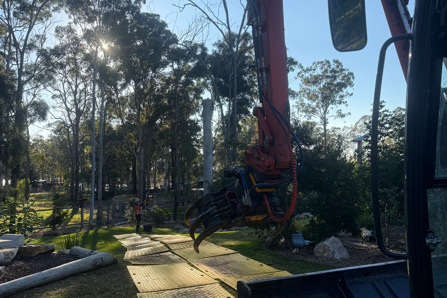 8-tonne excavator crossing temporary access mats to protect the lawn during commercial tree removal in Taree, NSW.