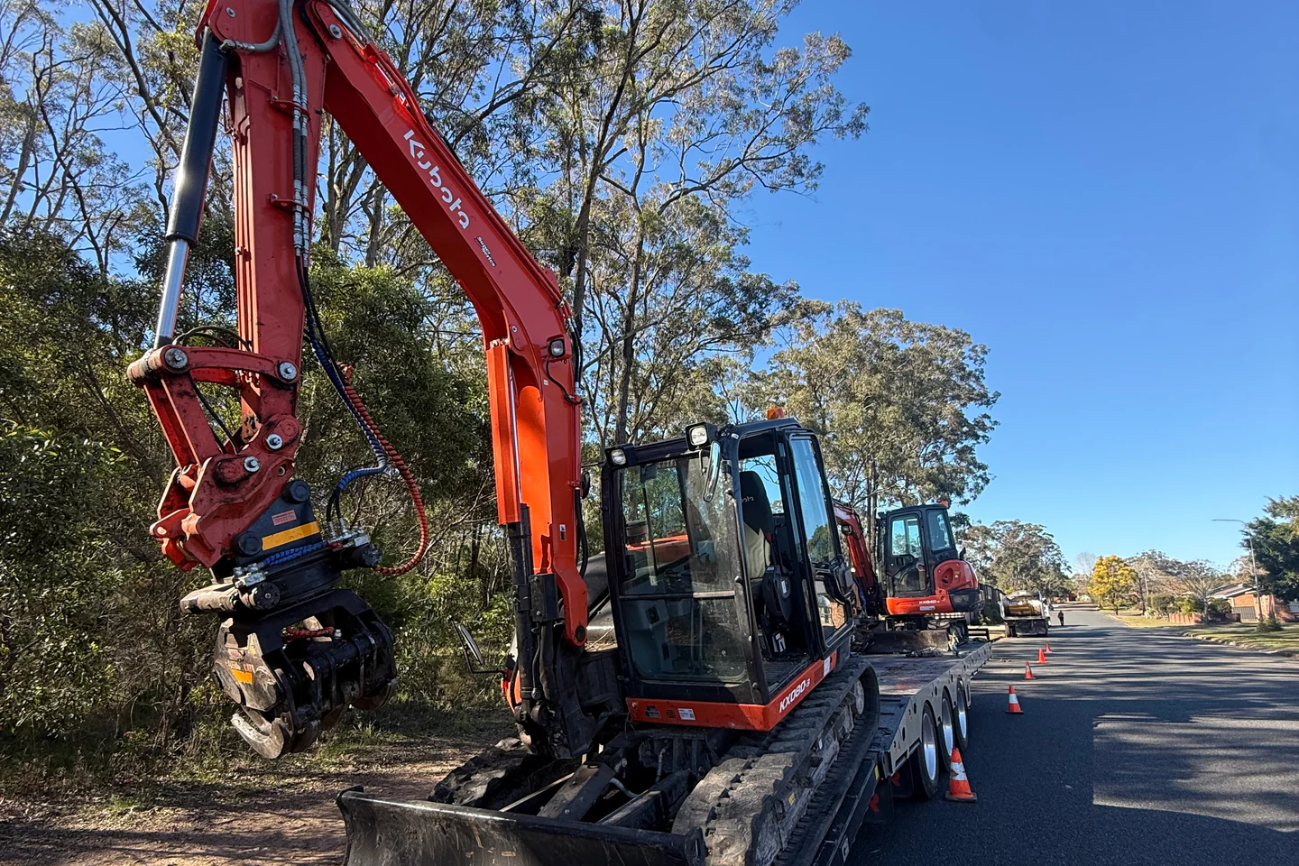 Excavator and attachments loaded on a trailer, ready for a fully insured arborist's next tree removal job.