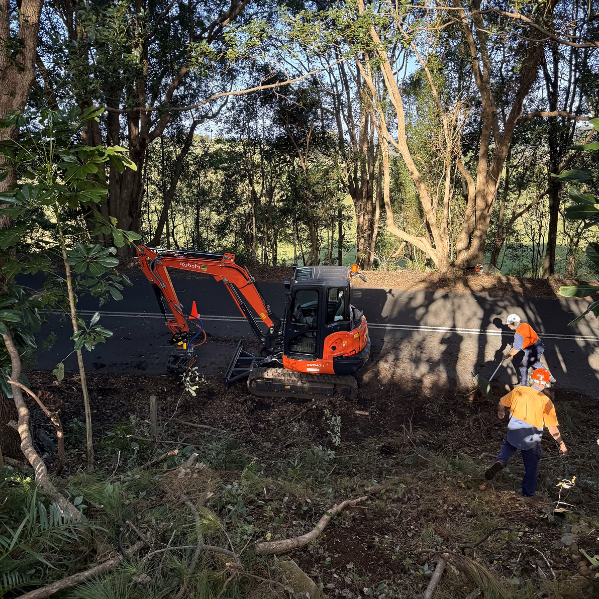MidCoast Tree Solutions crew in hi-vis clearing a roadside embankment while an excavator works below