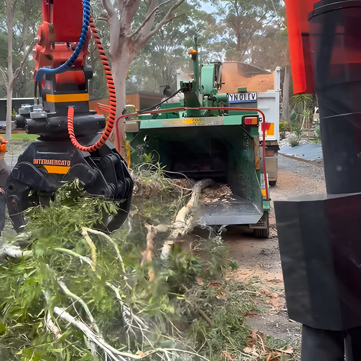 Excavator grapple feeding cleared boundary vegetation into a wood chipper